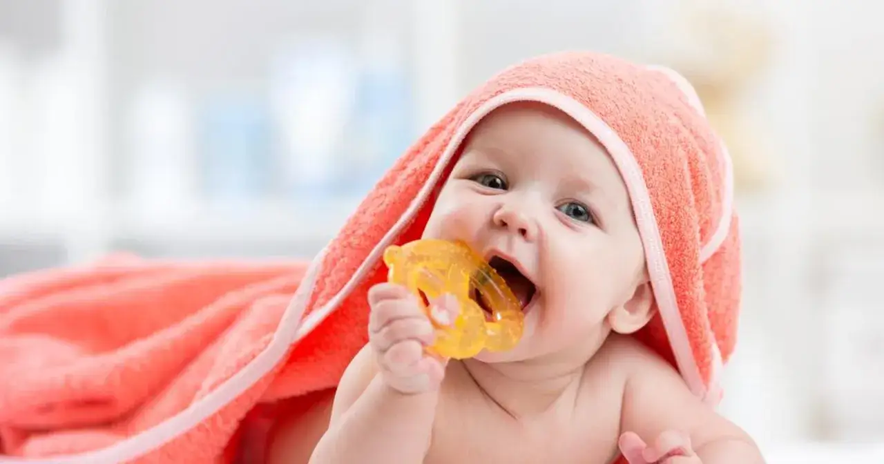 Maluch z pomarańczowym ręcznikiem na głowie gryzie ż&oacute;łtą zabawkę. To typowe ząbkowanie objawy, kt&oacute;re przynoszą ulgę.