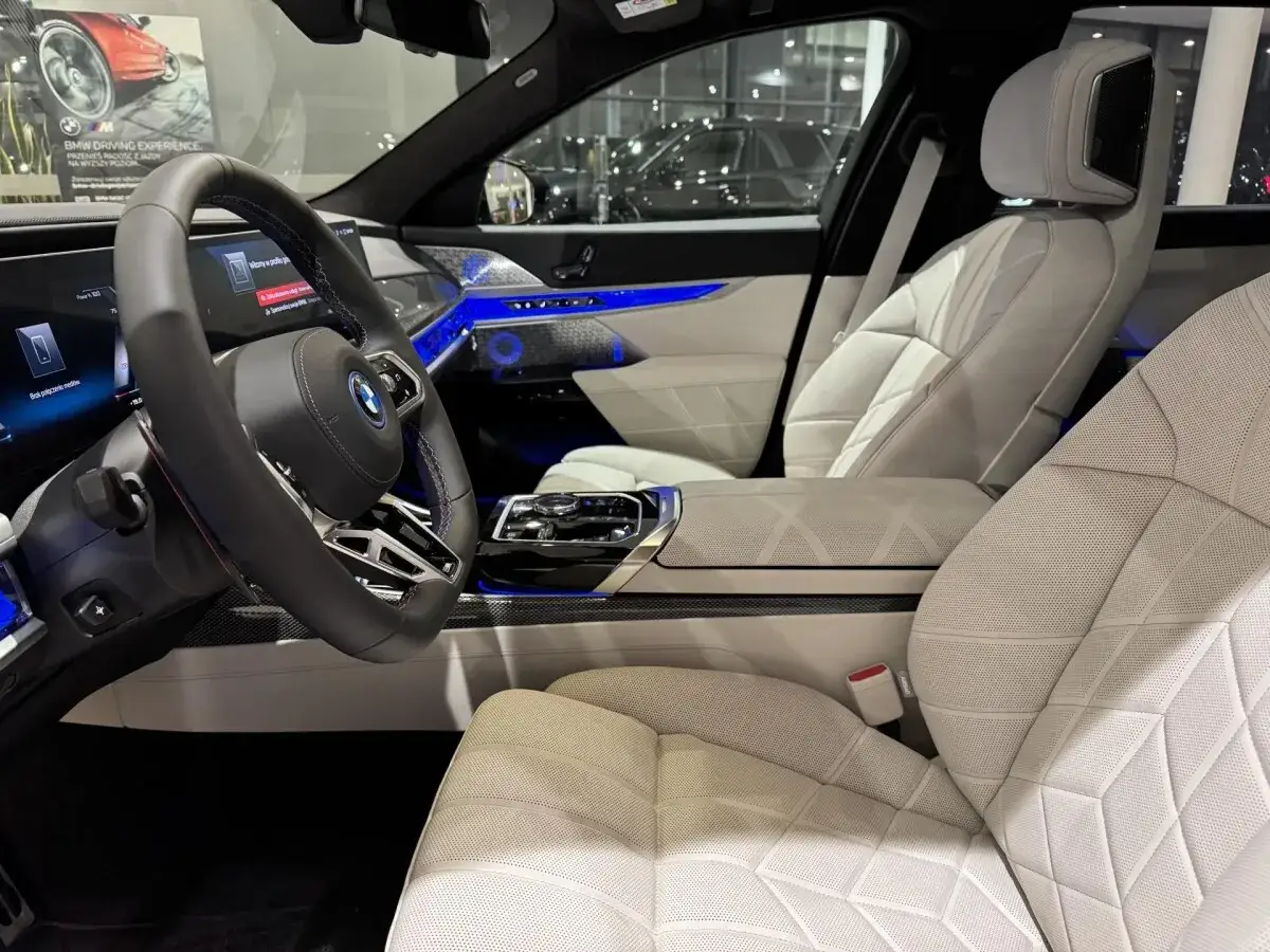 Wnętrze nowego BMW Serii 7 z białymi, pikowanymi fotelami i niebieskim ambientowym oświetleniem. Zastanawiasz się, ile kosztuje nowe BMW 7?