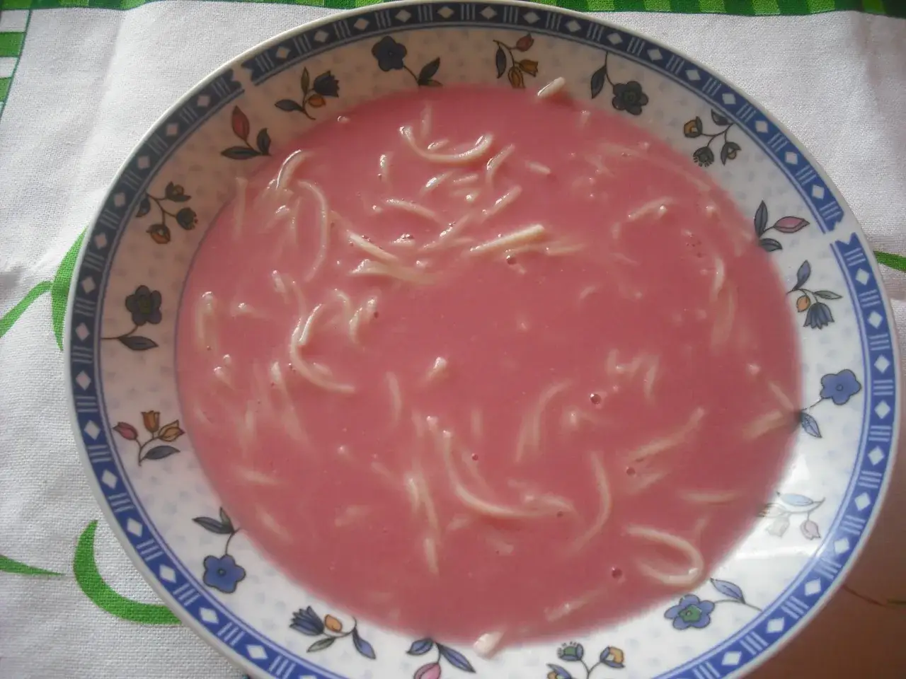 R&oacute;żowa zupa owocowa z makaronem w talerzu z kwiatowym wzorem. Pyszne danie na lato.