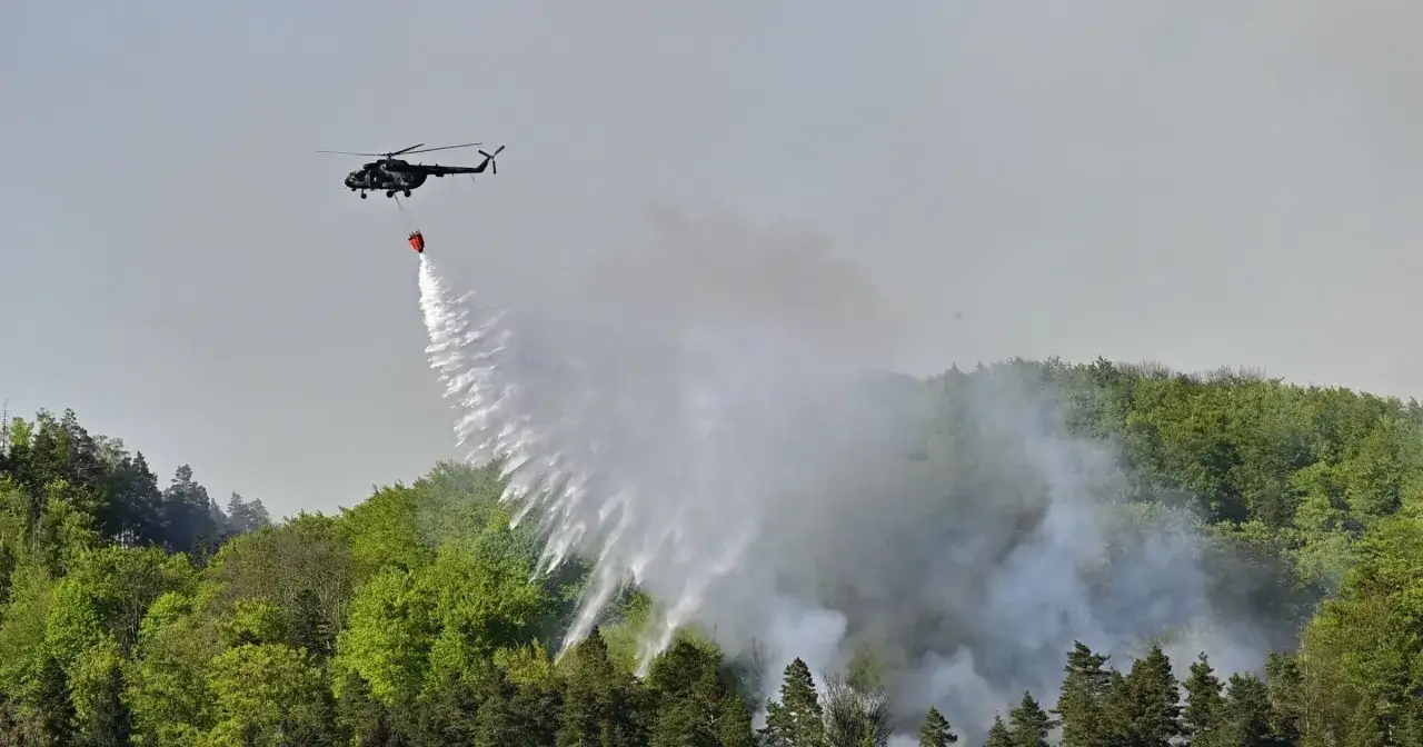 Helikopter gaśniczy zrzuca wodę na las w czeskiej Saksonii, walcząc z pożarem.