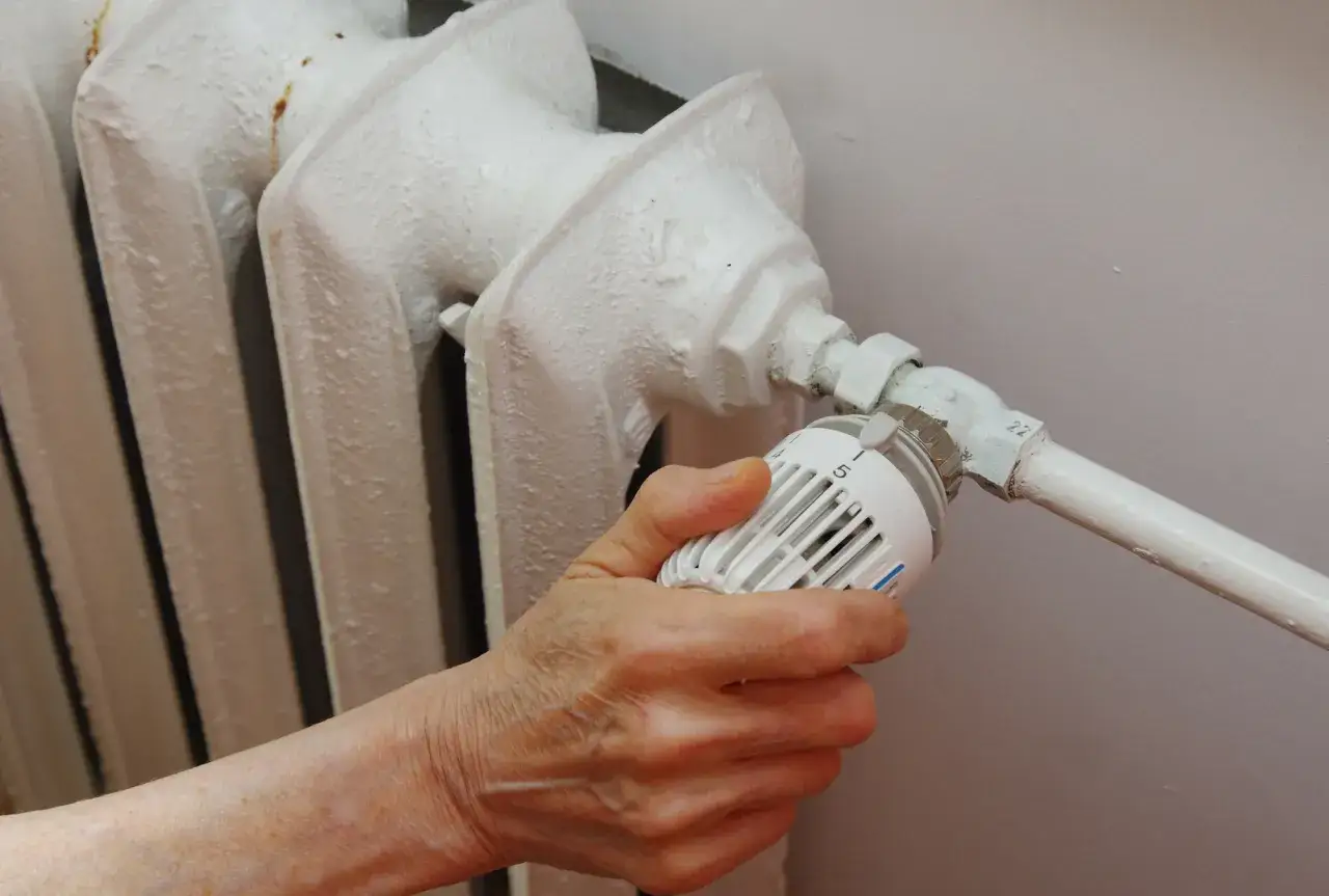 Dłoń reguluje termostat grzejnika. W obliczu rosnących cen energii, dopłaty do węgla stają się kluczowe dla wielu gospodarstw domowych.