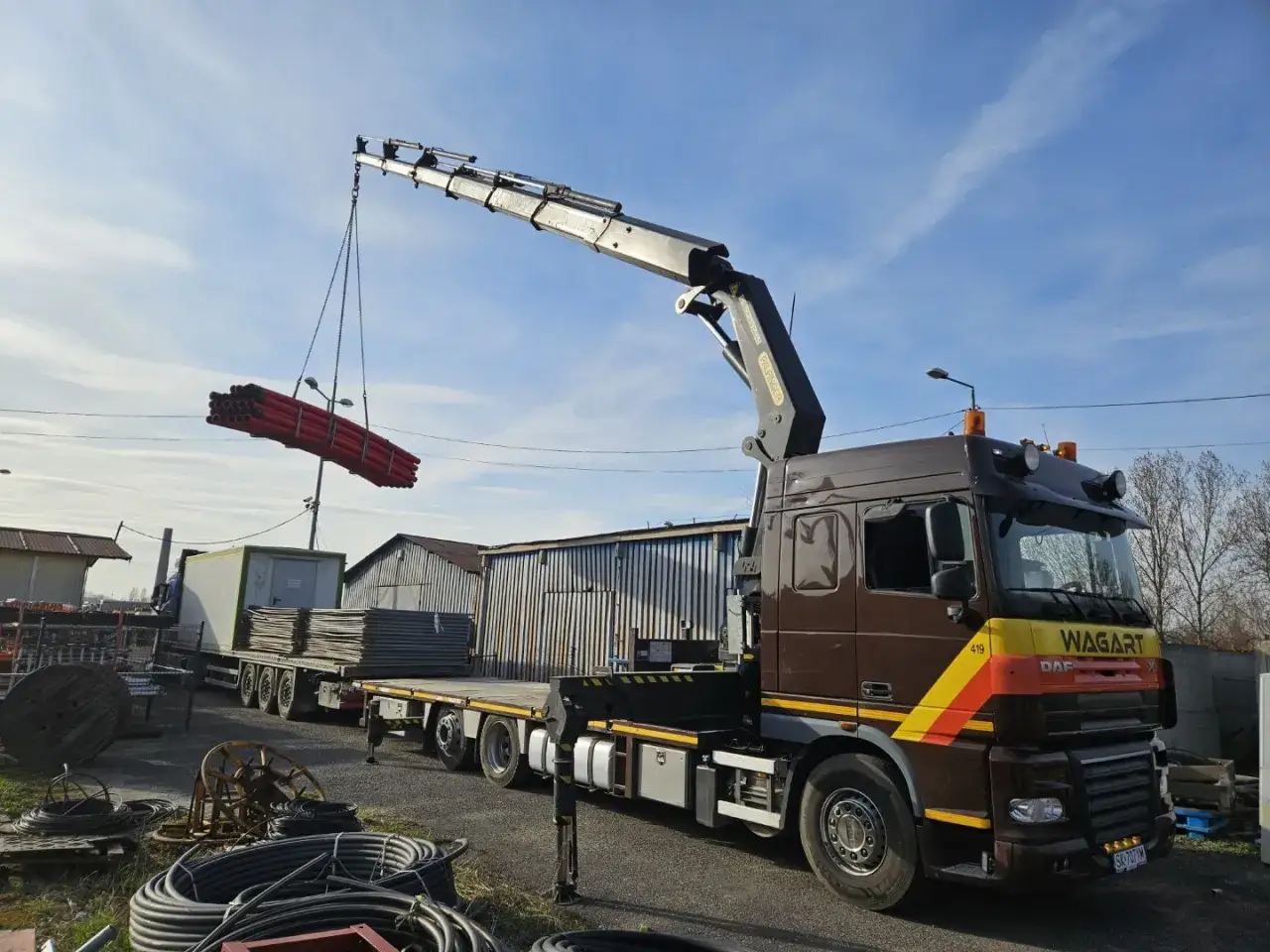 Ciężarówka z HDS rozładowuje czerwone rury w CBN Centrum Budowlane oddział Śledziejowice.