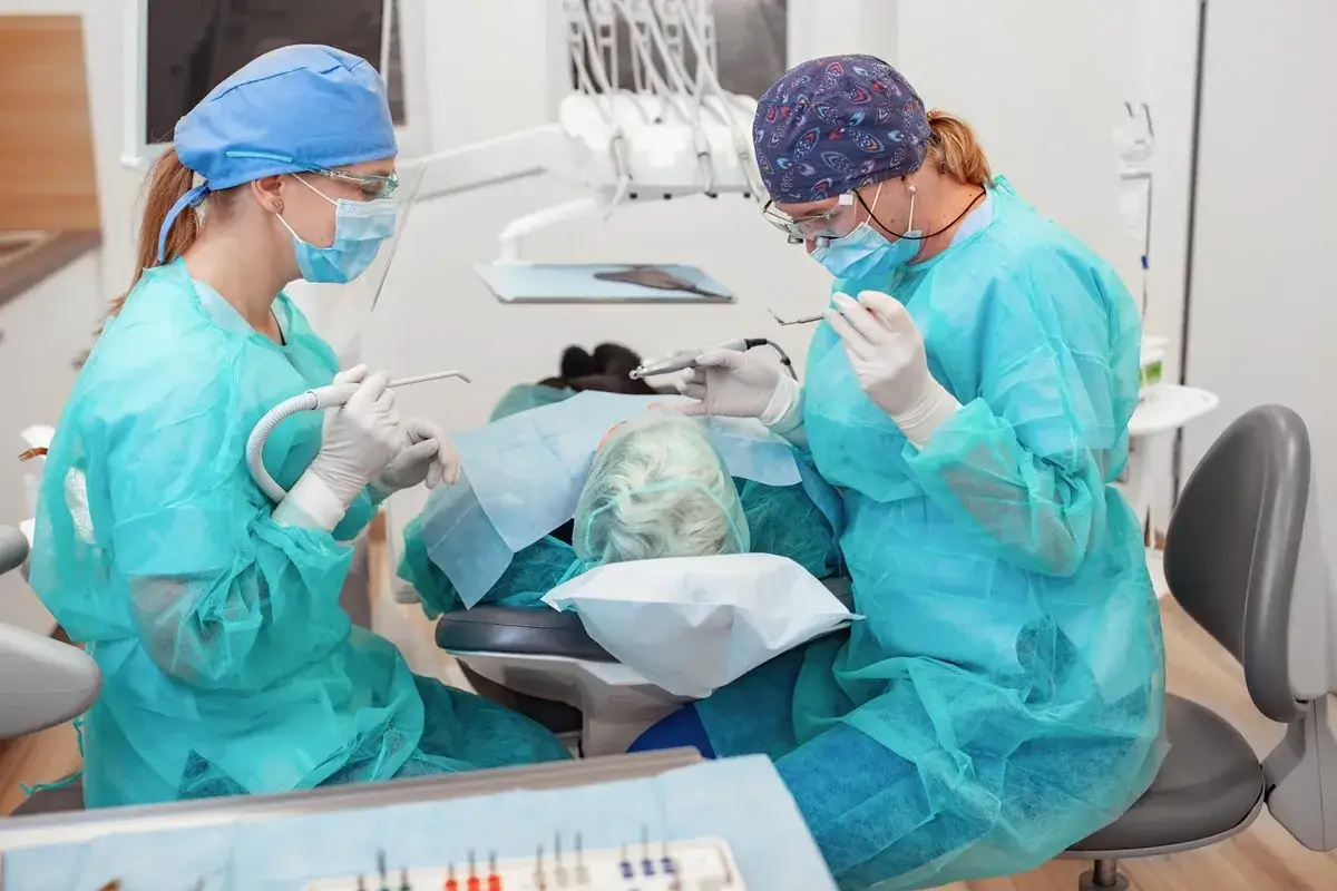 Dwie dentystki w maseczkach i fartuchach ratują pacjentkę, która cierpi gdzie z bólem zęba w weekend.