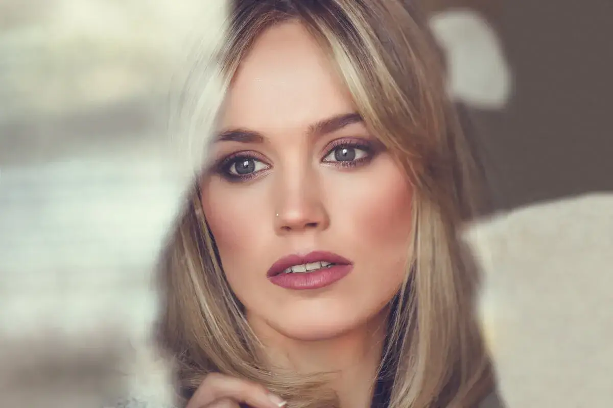 Blondynka z wysokim czołem, wpatrzona w dal, z subtelnym makijażem i kolczykiem w nosie.