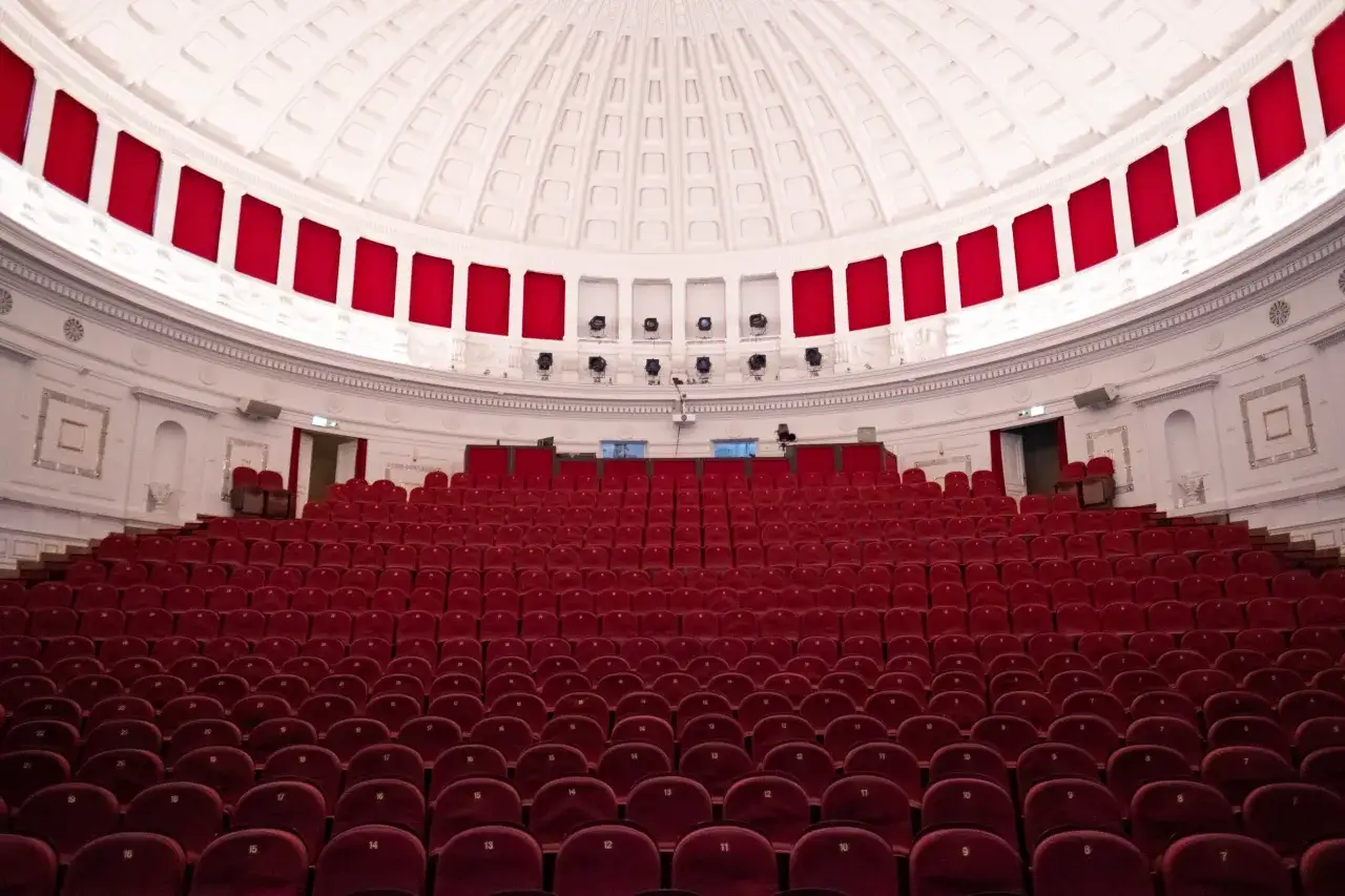 Puste czerwone fotele teatralne czekają na widzów najlepszych spektakli komediowych. Wnętrze z kopułą i czerwonymi zasłonami.