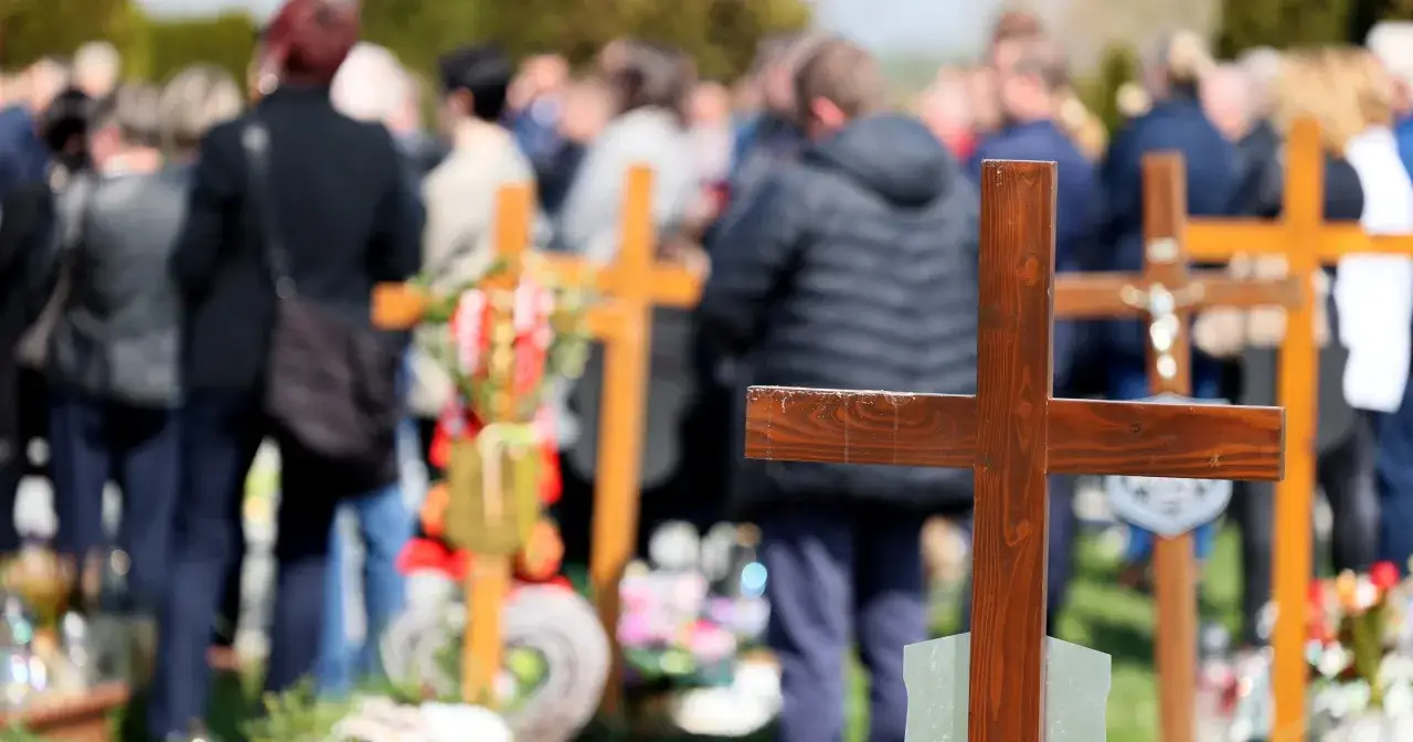 Uroczystość pogrzebowa z krzyżami i ludźmi w tle. Ile daje się księdzu za pogrzeb? To pytanie często zadawane w takich chwilach.