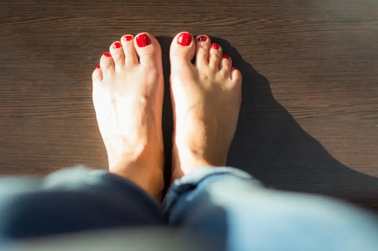 Dwie stopy z czerwonym lakierem na paznokciach na ciemnym tle. Moczenie nóg w sodzie na co pomaga? Na zmęczone stopy i odświeżenie.