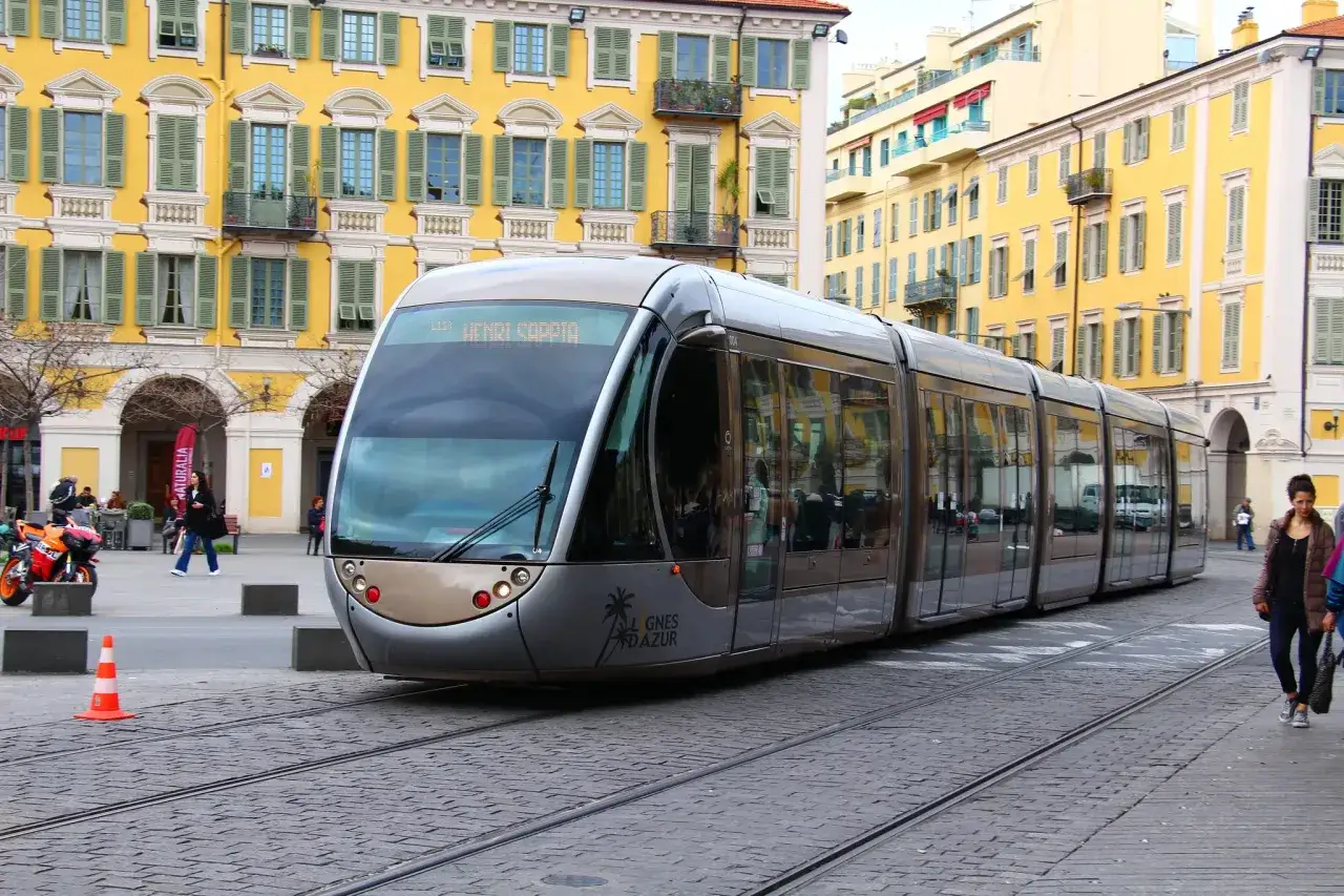 Tram na Lazurowym Wybrzeżu w Nicei, z żółtymi budynkami w tle.
