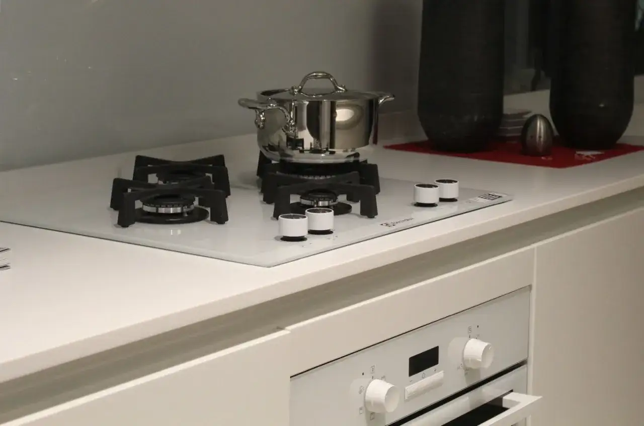 Nowoczesna biała płyta gazowa z garnkiem w trakcie montażu. Eleganckie pokrętła i czarne palniki.