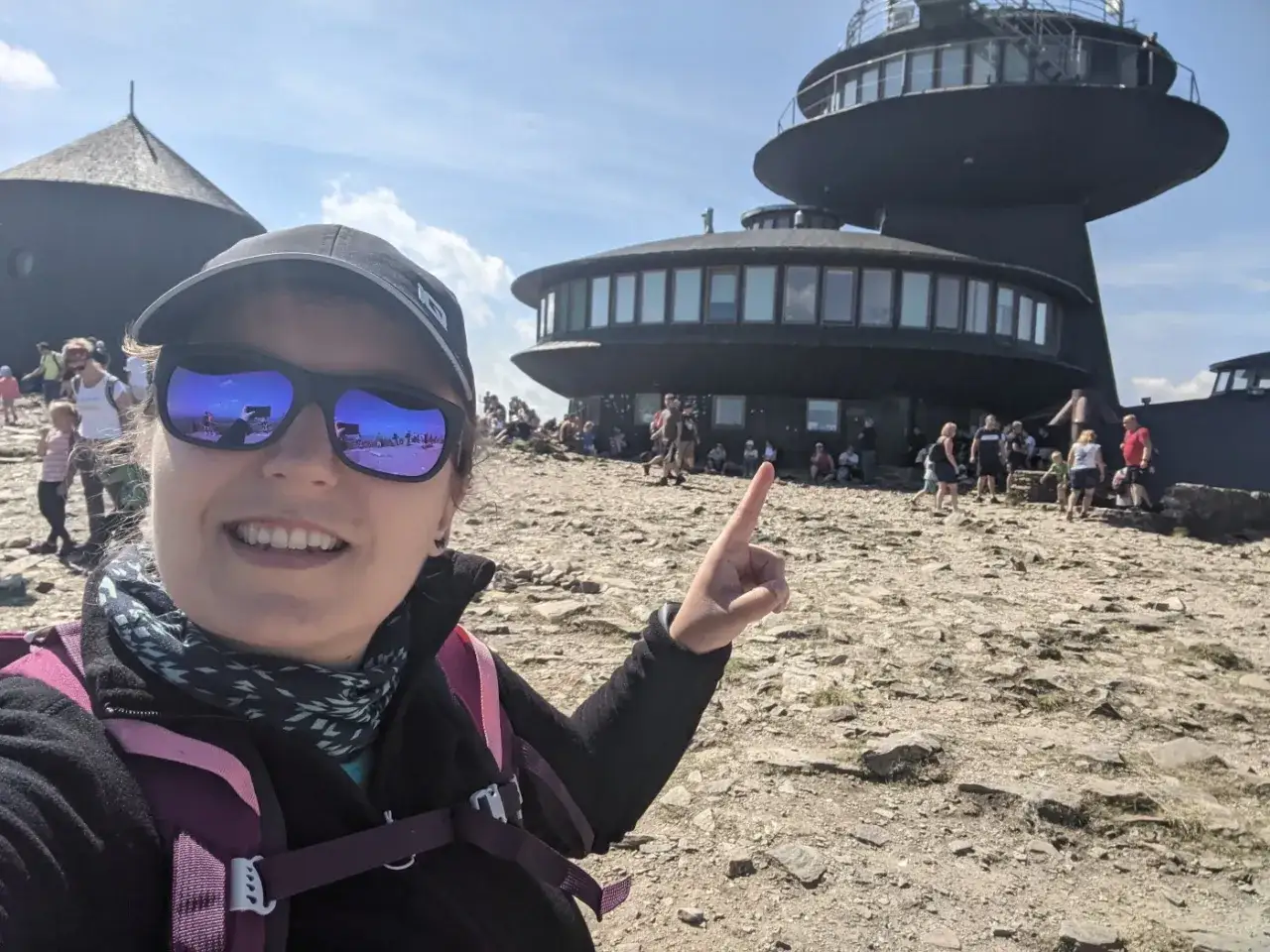 Kobieta na szczycie Śnieżki, wskazując na budynek. Może to być cel podr&oacute;ży, jeśli szukasz, jaki jest najłatwiejszy szlak na Śnieżkę.