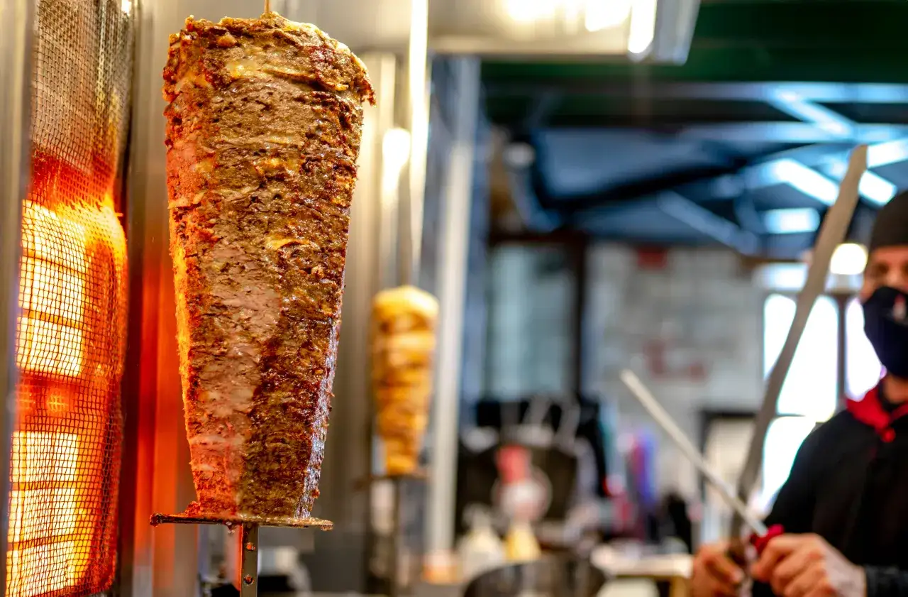 Duży, obracający się pionowo kebab, pieczony na ogniu. Widać warstwy soczystego mięsa, które zaraz zostaną odkrojone. To idealny kebab, jakie mięso wybrać?