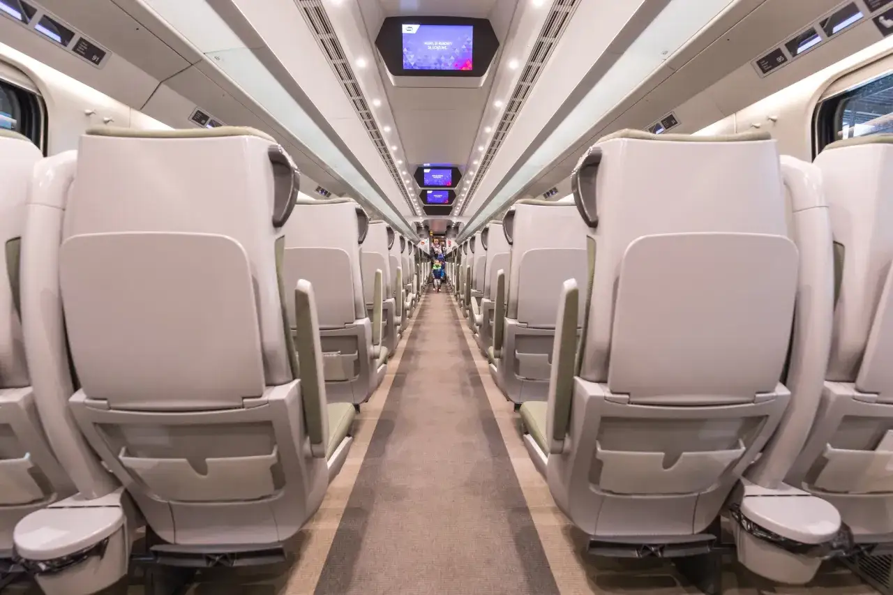 Wnętrze nowoczesnego pociągu, rzędy jasnych siedzeń po obu stronach korytarza. Czy pociąg EIP to Pendolino? Tak, to właśnie Pendolino.