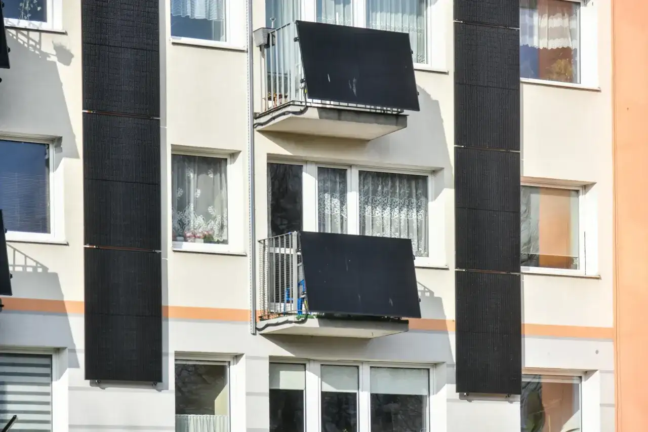 Panele fotowoltaiczne na balkonie, zamontowane na ścianie bloku, zbierają energię słoneczną.