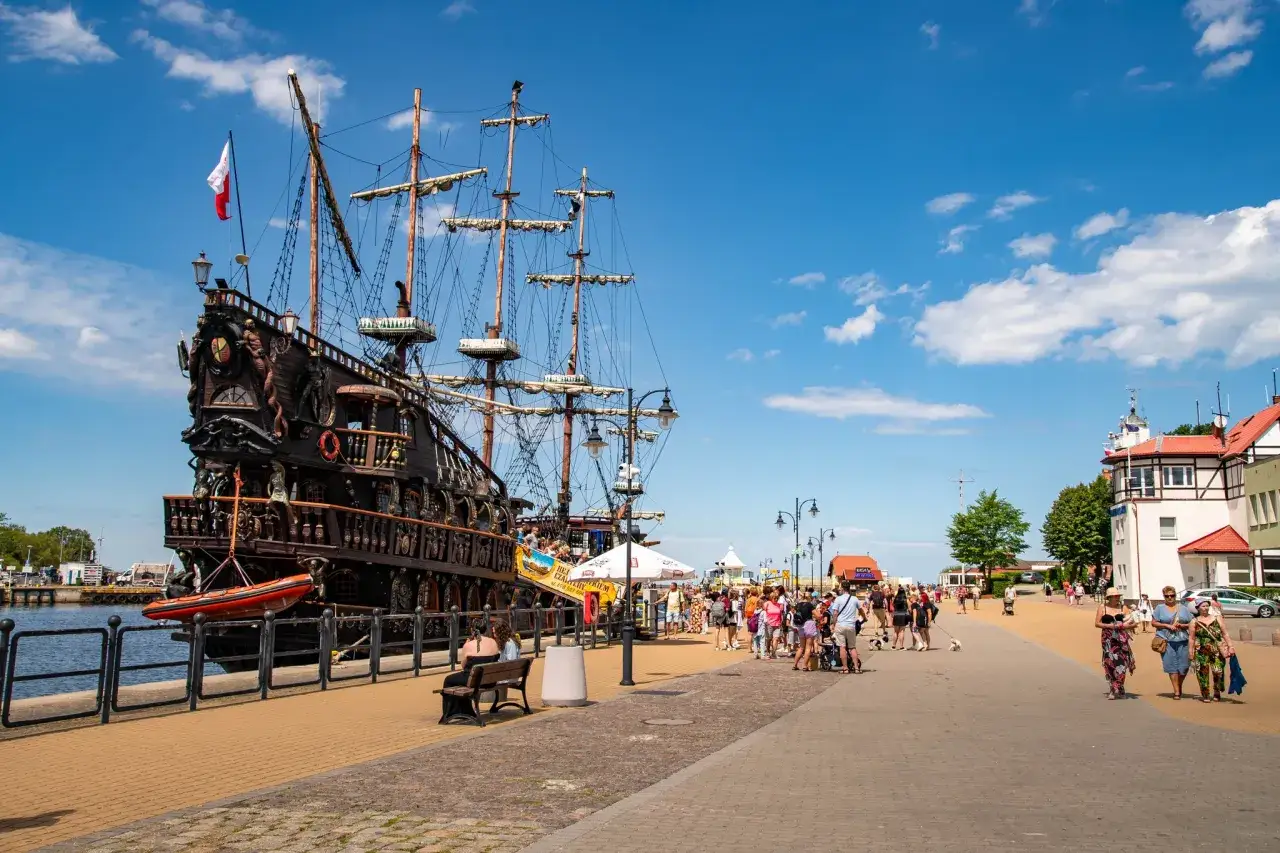 Portowe miasteczka obok Ustki tętnią życiem. Na pierwszym planie zacumowany statek piracki, a w tle spacerujący turyści.