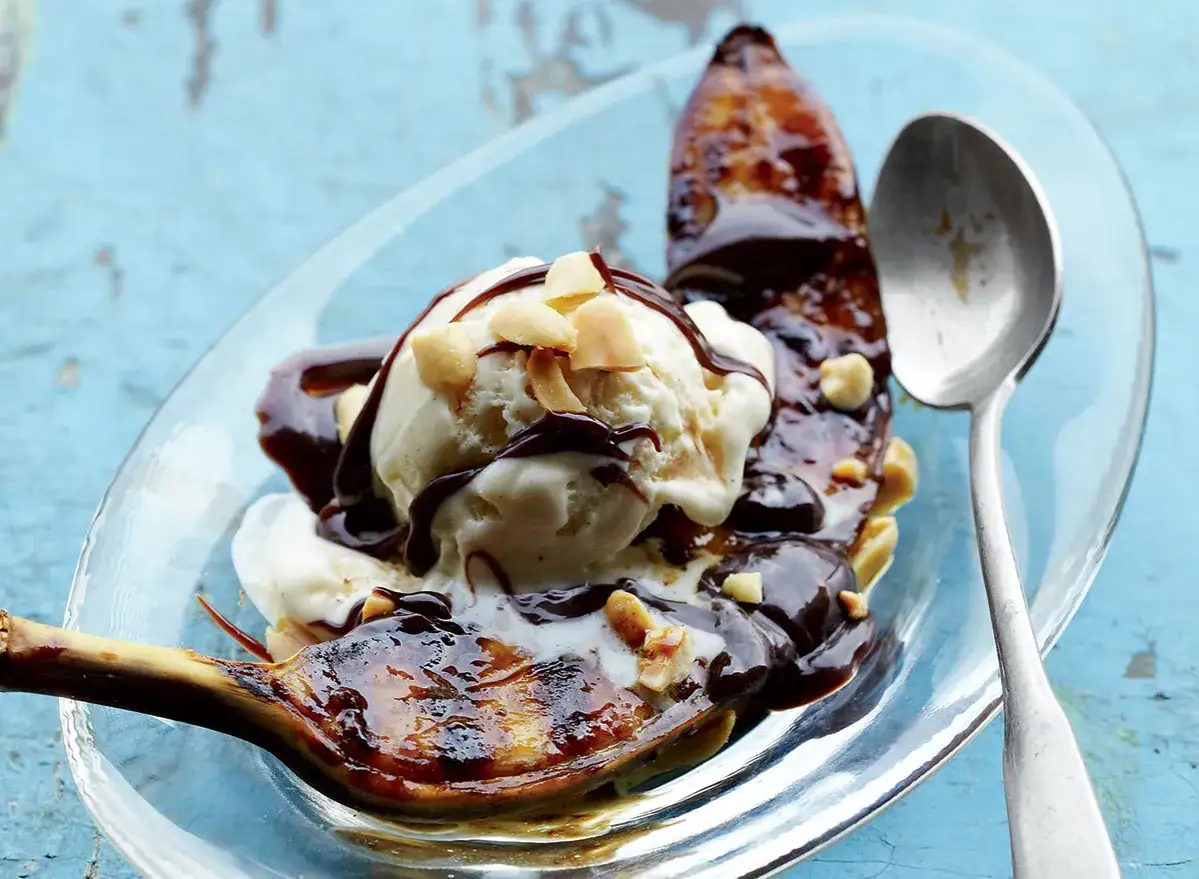 Grillowane banany z czekoladą i lodami waniliowymi, posypane orzechami. Pyszny deser na talerzu.
