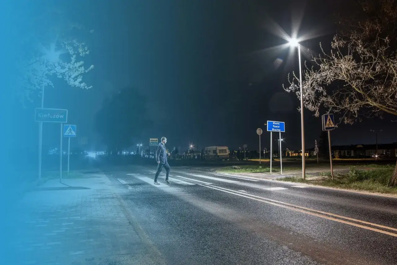 Mężczyzna przechodzi przez pasy nocą, oświetlony latarnią. To miejsce wymaga audytu oświetlenia, by zapewnić bezpieczeństwo.