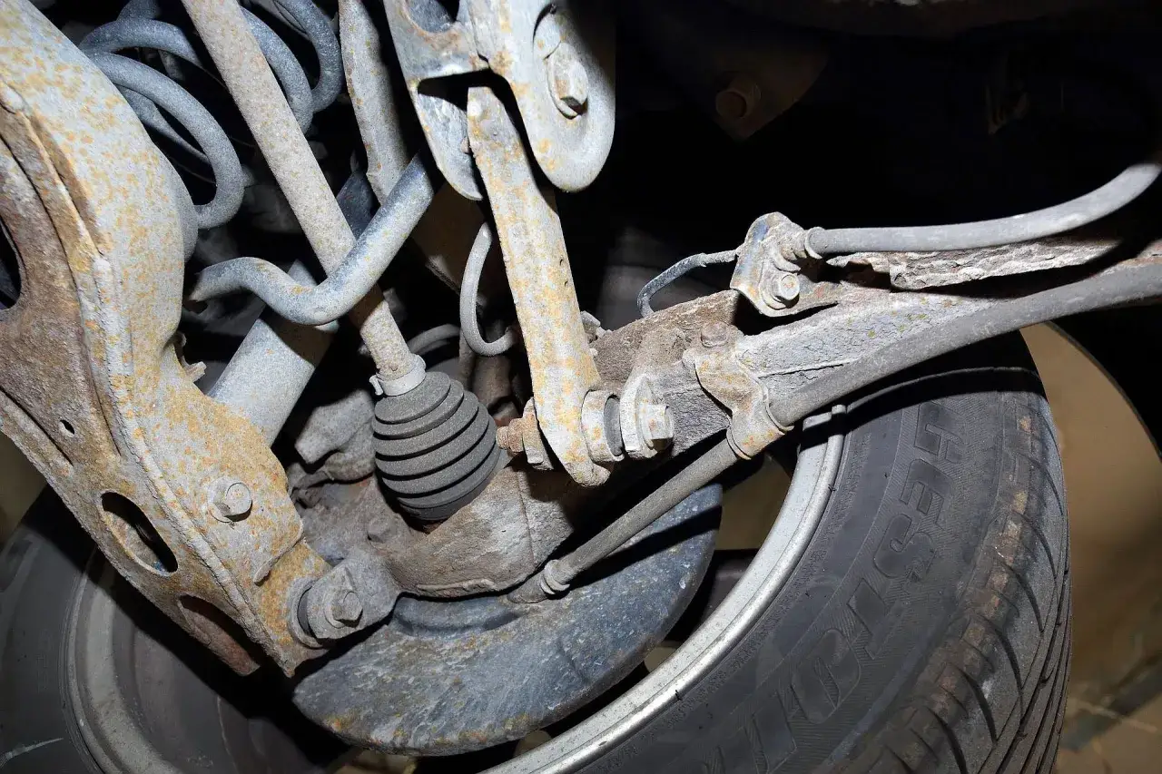 Widok z dołu samochodu na skorodowane elementy zawieszenia i oponę. Może to być przyczyna skrzypienia przy skręcaniu.