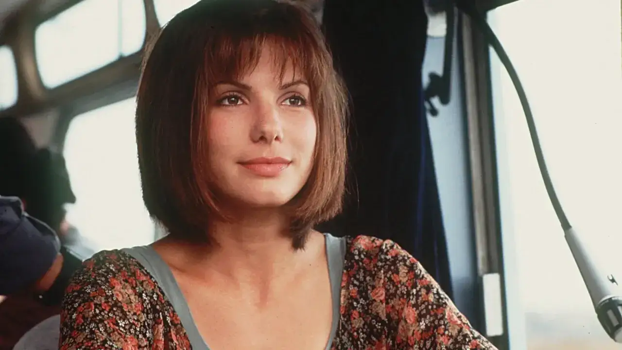 Sandra Bullock, której pochodzenie jest fascynujące, w kwiecistej bluzce, zamyślona.