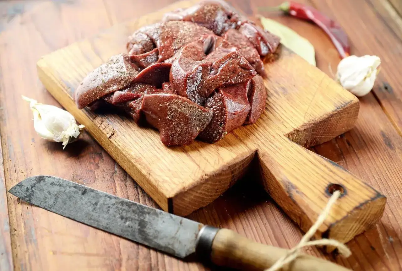 Wątróbka, bogata w witaminę PP, czeka na przygotowanie. Obok czosnek i nóż.