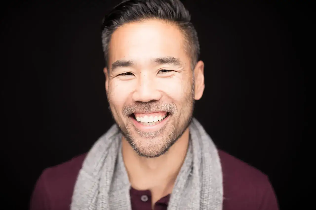 Mężczyzna z siwiejącymi włosami i zarostem uśmiecha się szeroko, pokazując białe zęby. Widać, jak się ładnie uśmiechać do zdjęć, z lekko zmrużonymi oczami.