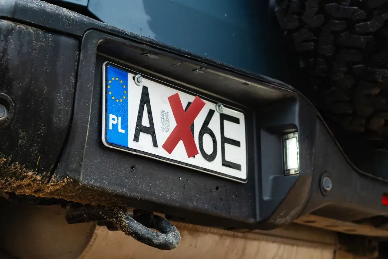 Polskie tablice rejestracyjne PL AX6E z czerwoną naklejką na literze X.