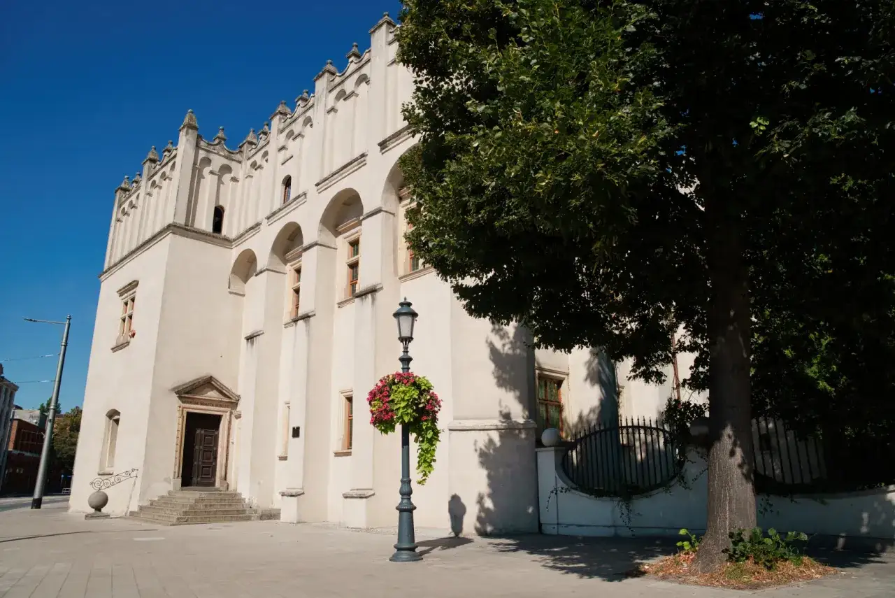 Zamek w Pabianicach, biała budowla z arkadowymi oknami, ozdobiona latarnią z kwiatami.