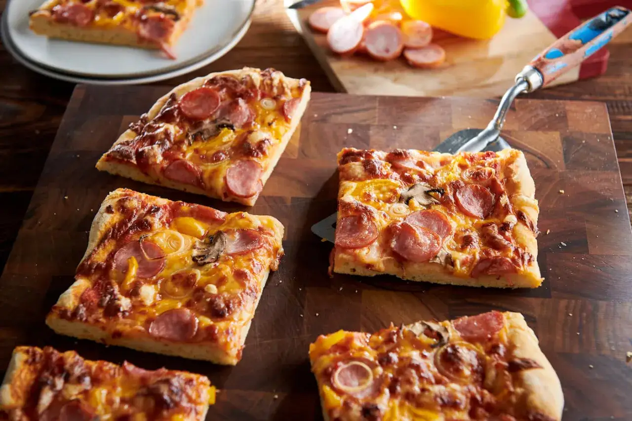 Kawałki pysznej pizzy z kiełbasą, pieczarkami i papryką na drewnianej desce.