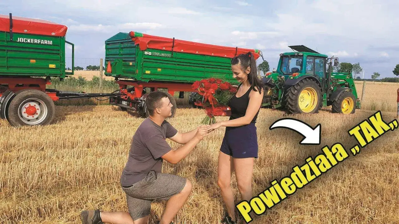 Na polu, gdzie mieszka Jockerfarm, mężczyzna klęczy i oświadcza się kobiecie z bukietem róż. W tle zielony traktor i przyczepy.