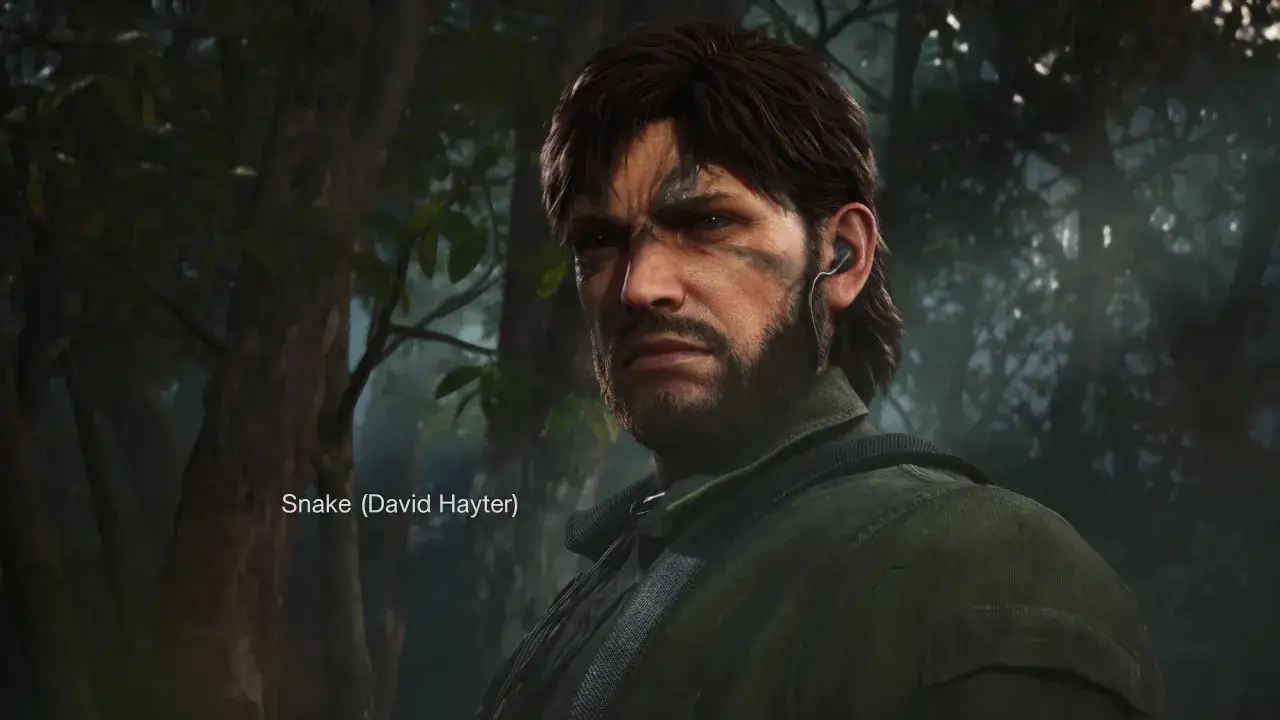 Solid Snake z gry Metal Gear Solid Delta, w zielonej kurtce, z charakterystycznym zarostem i opaską na uchu, stoi w lesie.