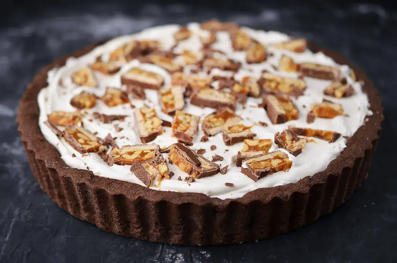 Czekoladowa tarta z kajmakiem i mascarpone, udekorowana kawałkami batoników. Idealna na deser!