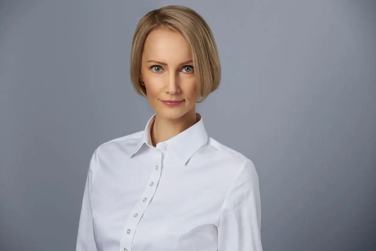 Kobieta w białej koszuli, z kr&oacute;tkimi blond włosami i niebieskimi oczami. Idealne tło do profilowego, emanuje profesjonalizmem i spokojem.