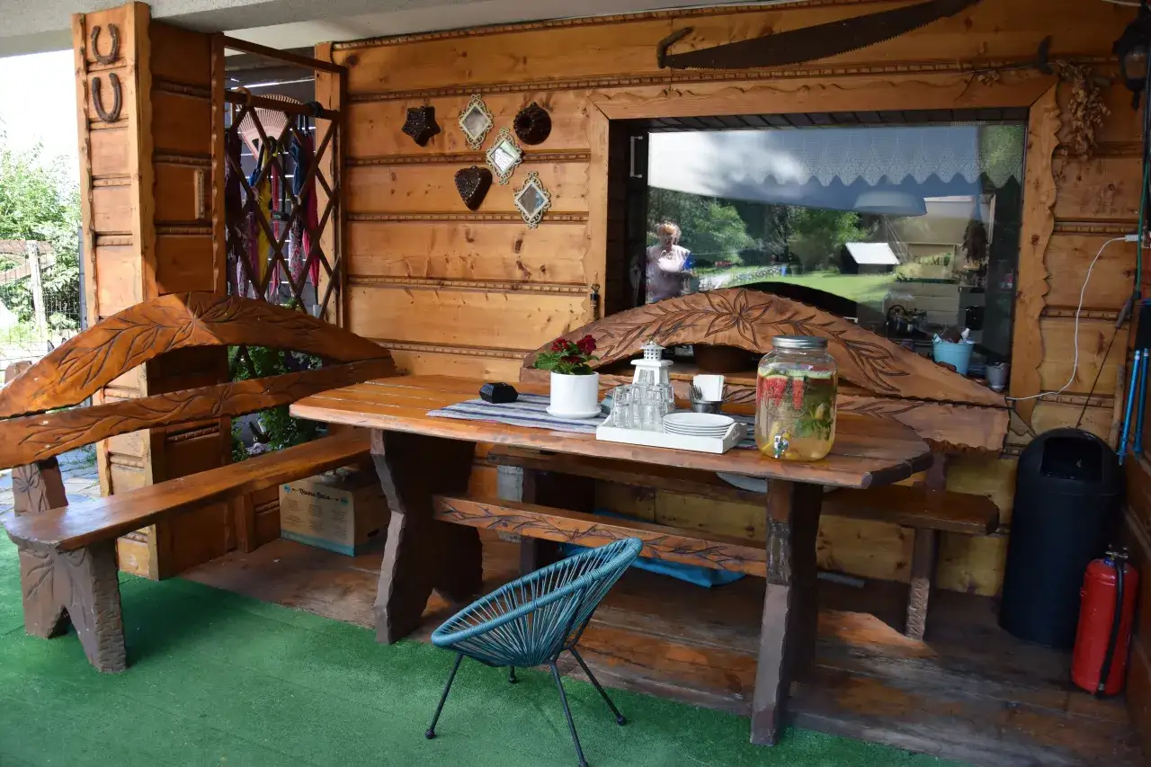 Drewniana altana w stylu agroturystyka bac&oacute;wka giemzik&oacute;w. St&oacute;ł z ławami, dzban z napojem, ozdoby na ścianie.