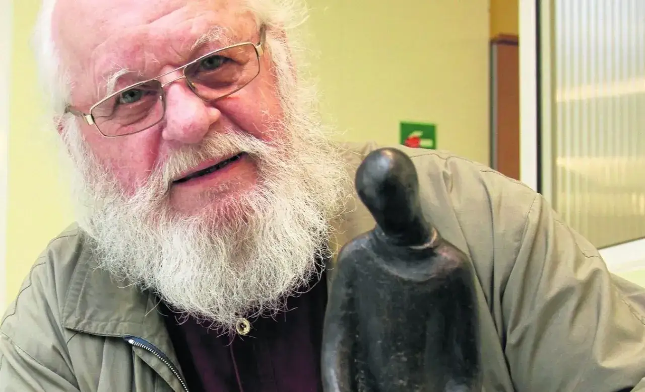 Aleksander Skowroński, z siwą brodą i w okularach, trzyma w dłoni małą, ciemną figurkę.