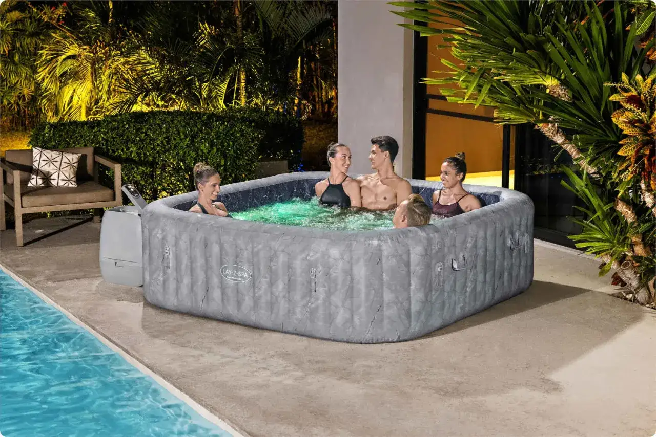 Grupa przyjaciół relaksuje się w dmuchanych basenach spa ogrodowych, ciesząc się ciepłą wodą i wieczornym klimatem.