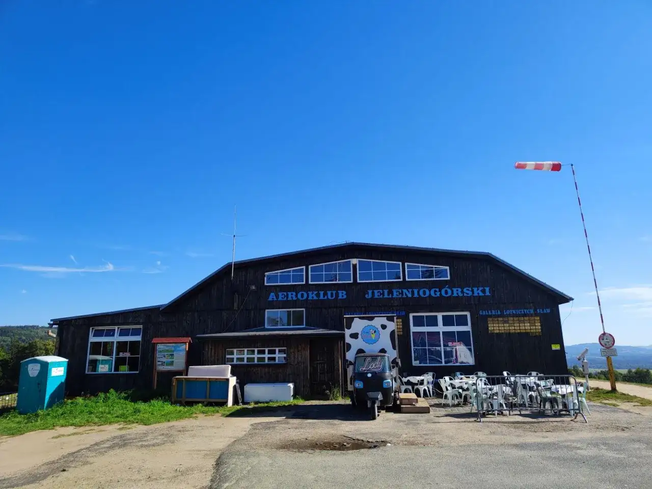 G&oacute;ra szybowcowa Jelenia G&oacute;ra. Aeroklub JelenioG&oacute;rski, mały pojazd i stoliki na zewnątrz. Jak dojechać?