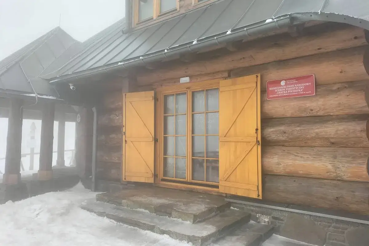 Drewniana chatka Puchatka w Bieszczadach, zasypana śniegiem, z żółtymi okiennicami.
