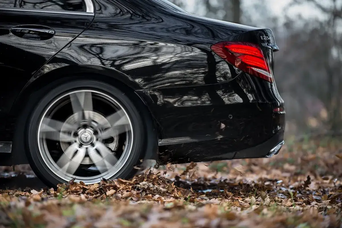 Błyszczący, czarny Mercedes-Benz Klasa E mija jesienne liście, koło w ruchu.
