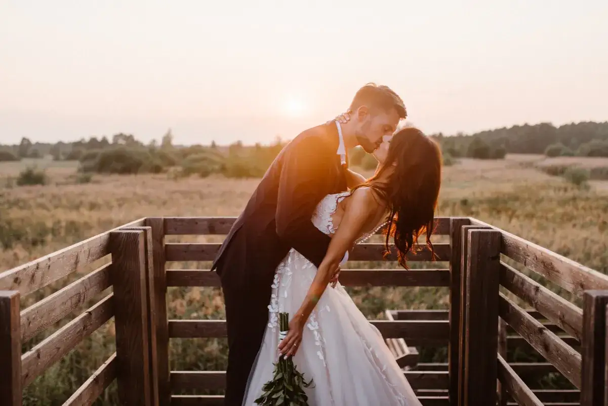 Romantyczna sesja zdjęciowa dla par. Młoda para całuje się na tle zachodzącego słońca, na drewnianym tarasie.