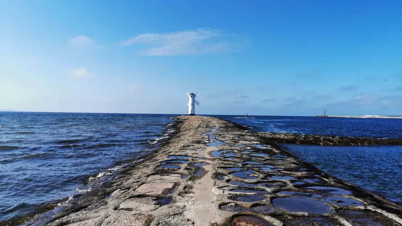 Kamienny falochron prowadzi do białej latarni w kształcie wiatraka. To jedno z miejsc, co warto zobaczyć w Świnoujściu, z pięknym widokiem na morze.