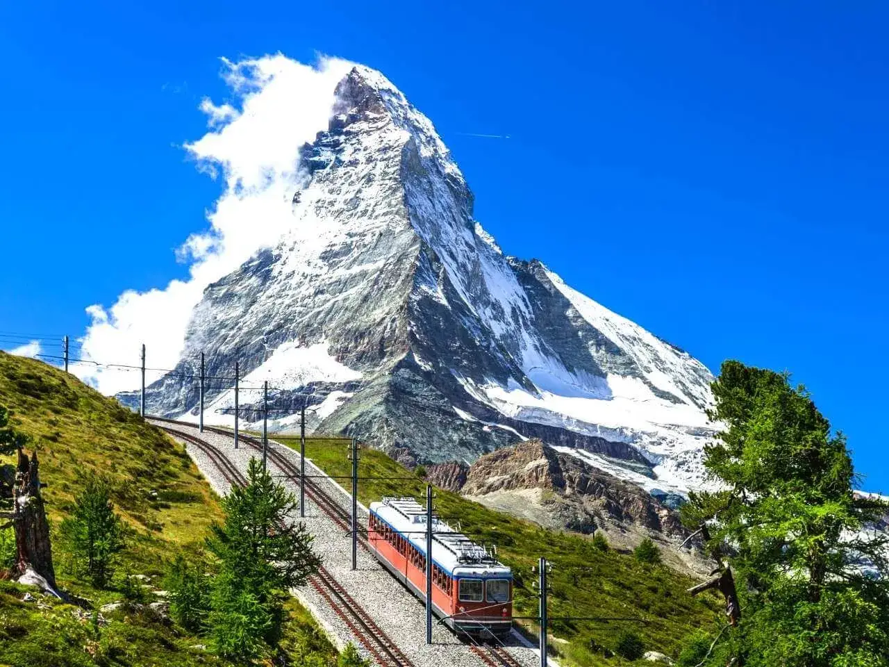 Widok na majestatyczne góry w Szwajcarii. Kolejka wjeżdża na zbocze, a w tle góruje ośnieżony szczyt.