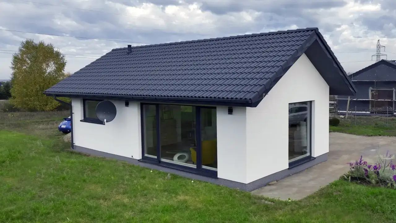 Nowoczesny biały dom modułowy z dużymi oknami i ciemnym dachem. Czy domy modułowe są trwałe? Ten wygląda solidnie.