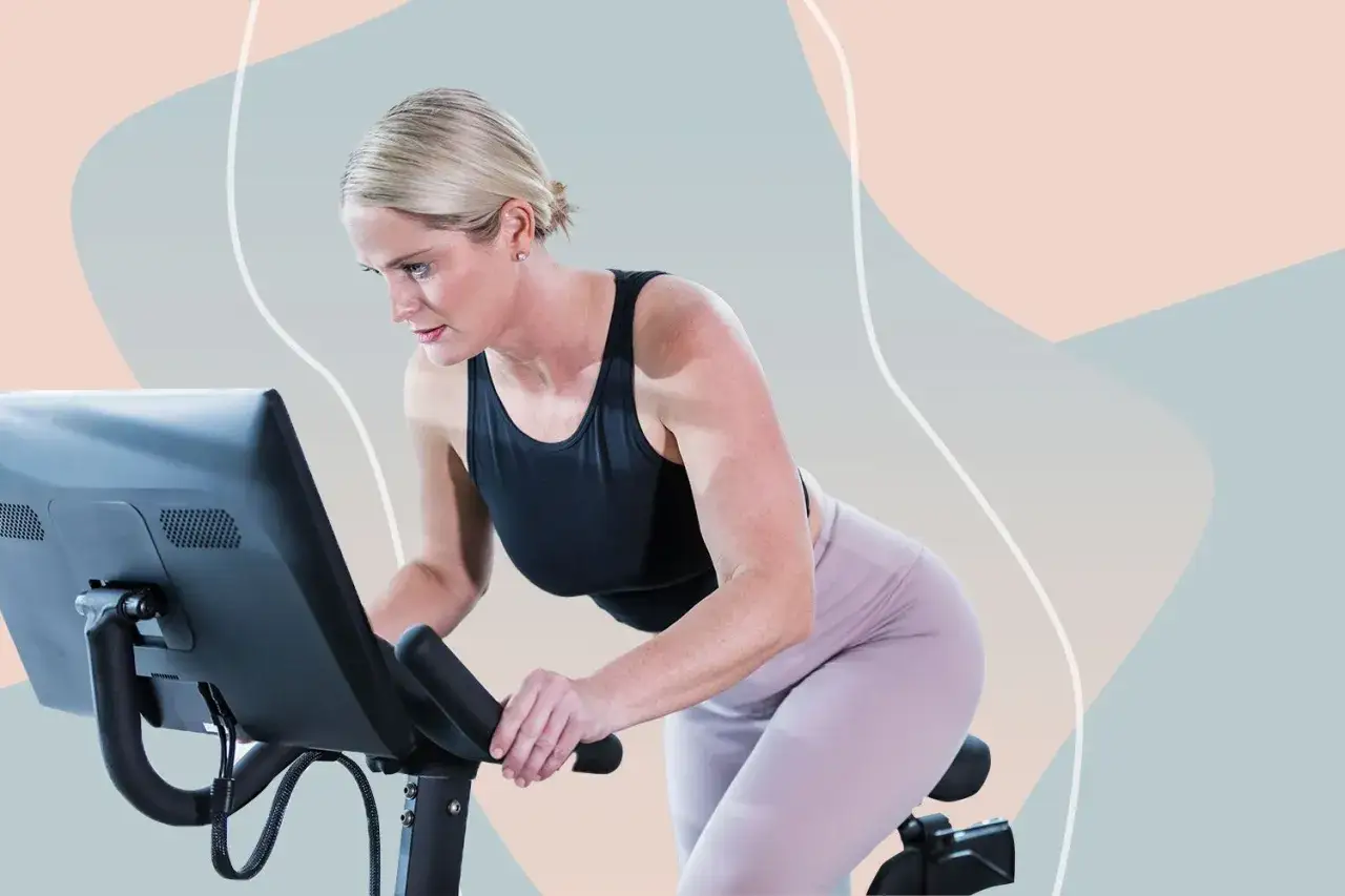 Kobieta w sportowym stroju intensywnie ćwiczy na rowerze stacjonarnym, skupiona na treningu.