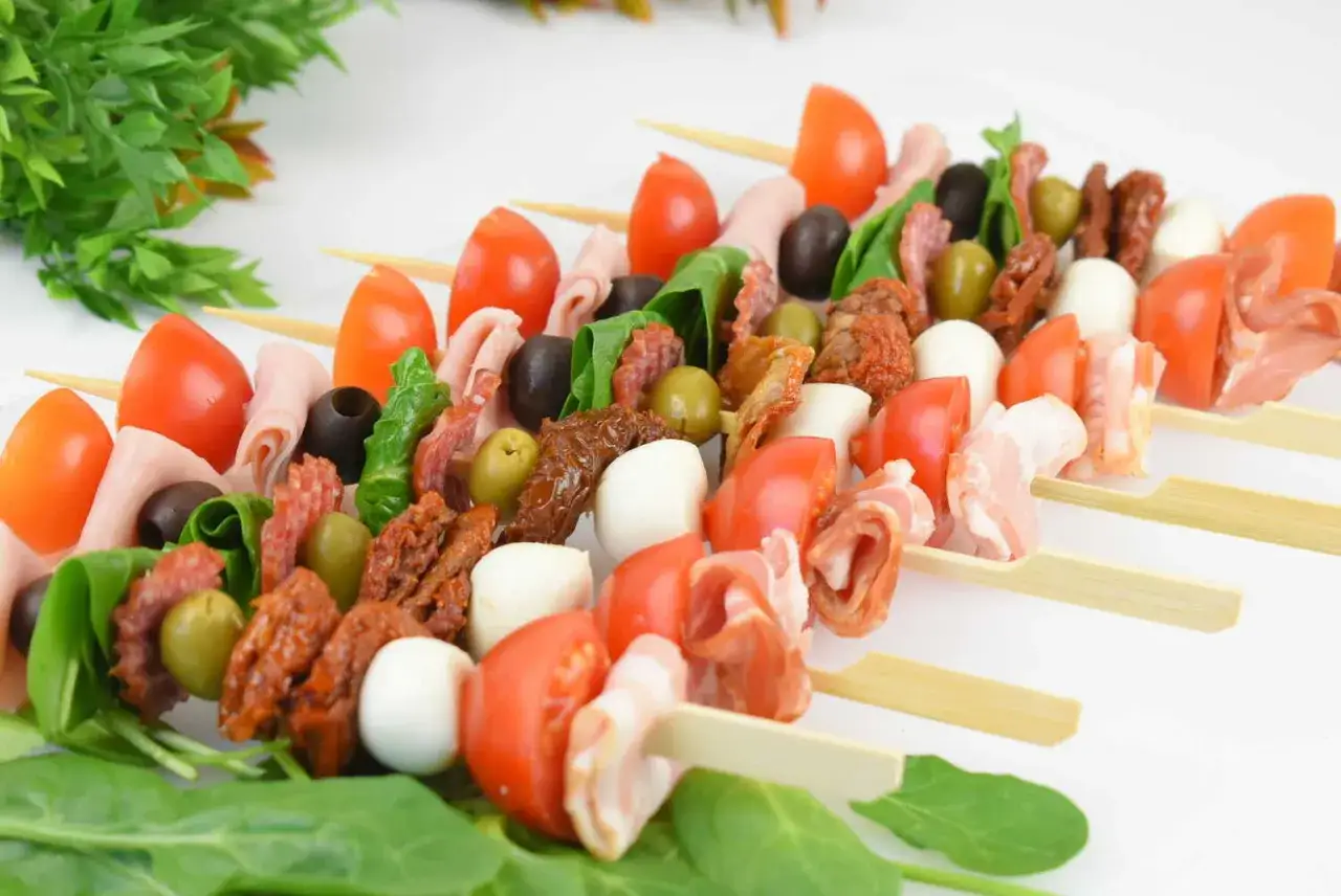 Kolorowe przystawki na grilla na patyczkach: pomidorki, oliwki, ser mozzarella, wędliny i suszone pomidory. Idealne na letnie przyjęcie.