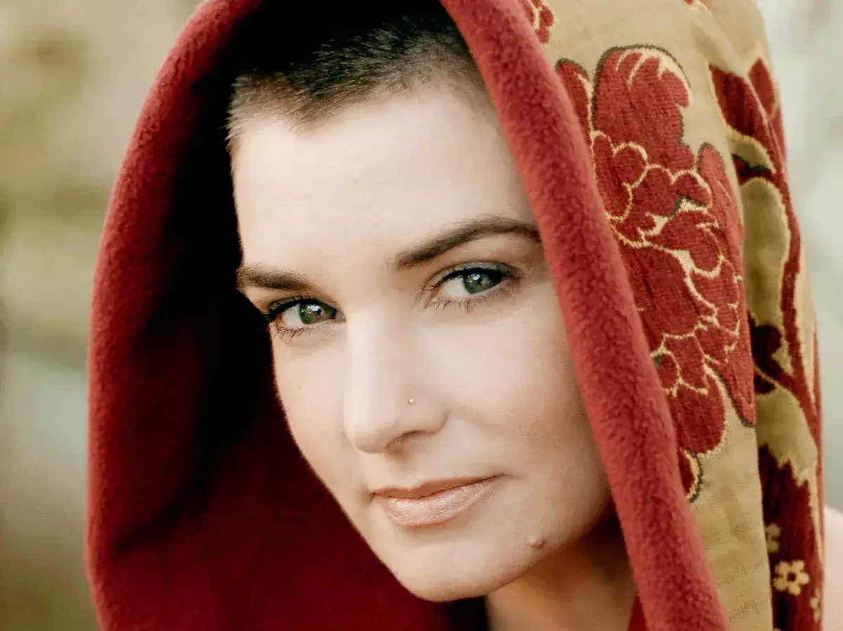 Twarz Sinéad O'Connor w kapturze z czerwonym obszyciem i wzorem kwiatowym. Jej utwory poruszają serca.
