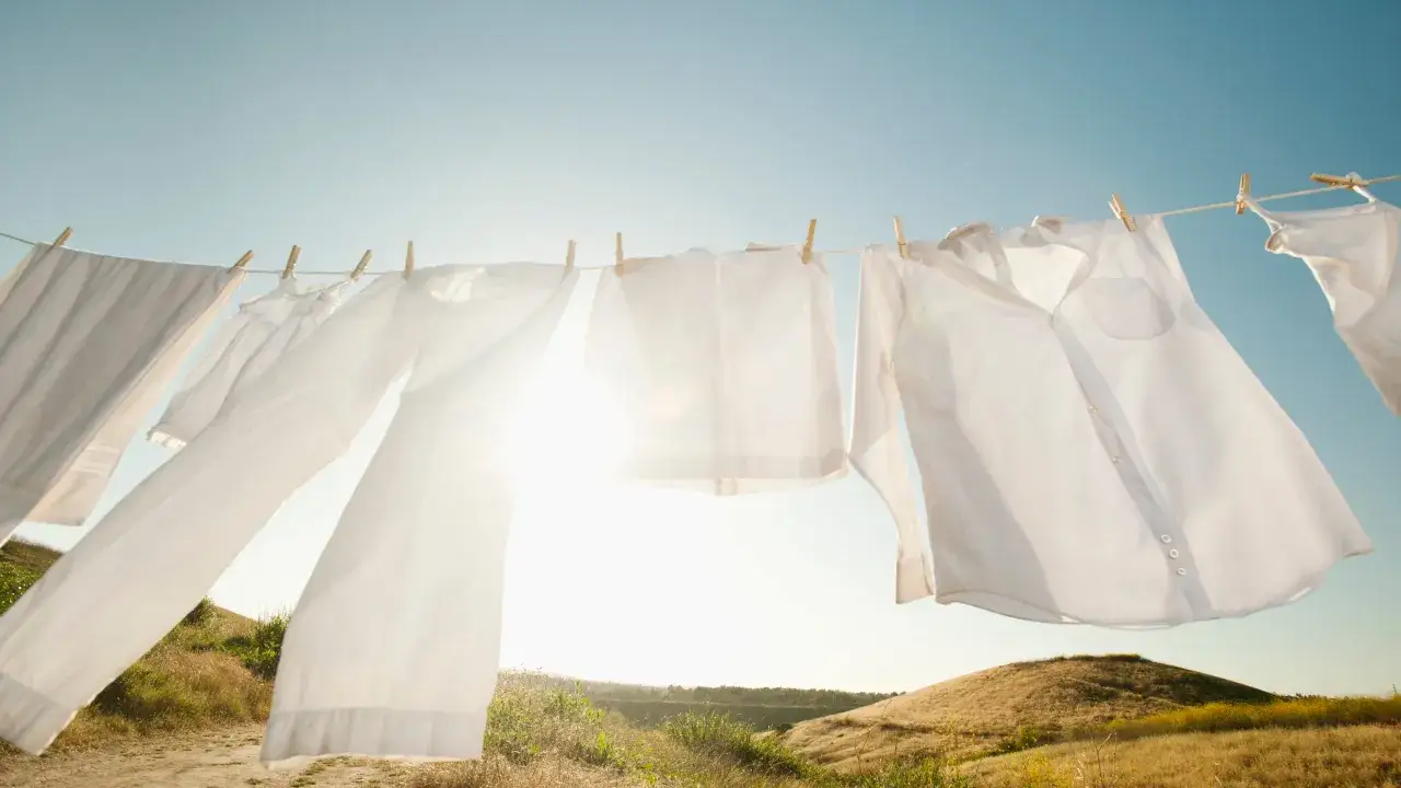 Białe ubrania schną na sznurku na tle błękitnego nieba i słonecznych wzgórz. Tak prac len, pachnący słońcem i świeżością.