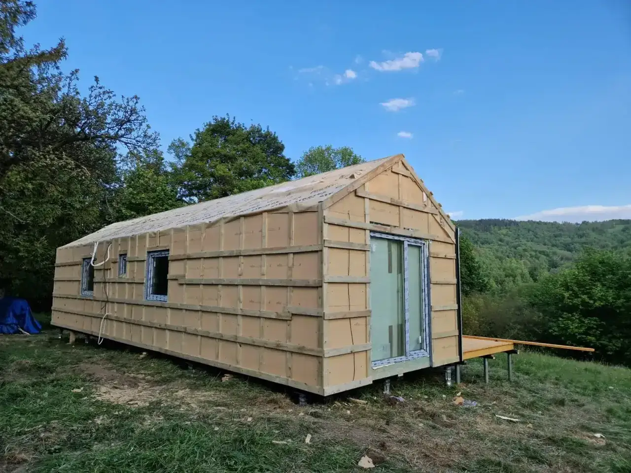 Budowa domku letniskowego na zgłoszenie w malowniczej okolicy. Konstrukcja z oknami i drzwiami tarasowymi, gotowa do dalszych prac.