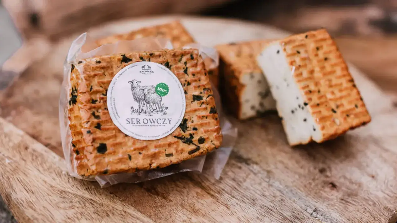 Tradycyjne bac&oacute;wka towary: ser owczy w opakowaniu z etykietą i kawałek sera z ziołami na desce.