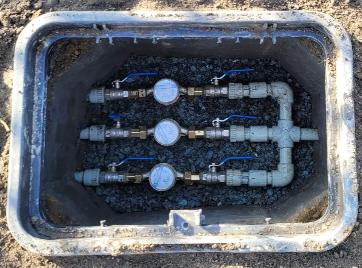 Trzy wodomierze z zaworami w skrzynce, sposób na to, jak zabezpieczyć wodomierz na działce przed mrozem i uszkodzeniem.