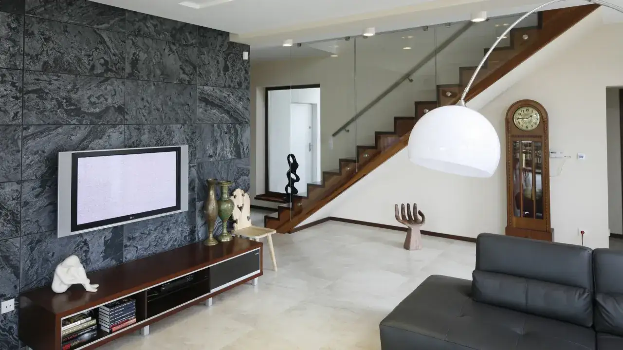 Nowoczesny salon z imponującą ścianą z kamienia, telewizorem, drewnianymi schodami i stylowymi meblami.