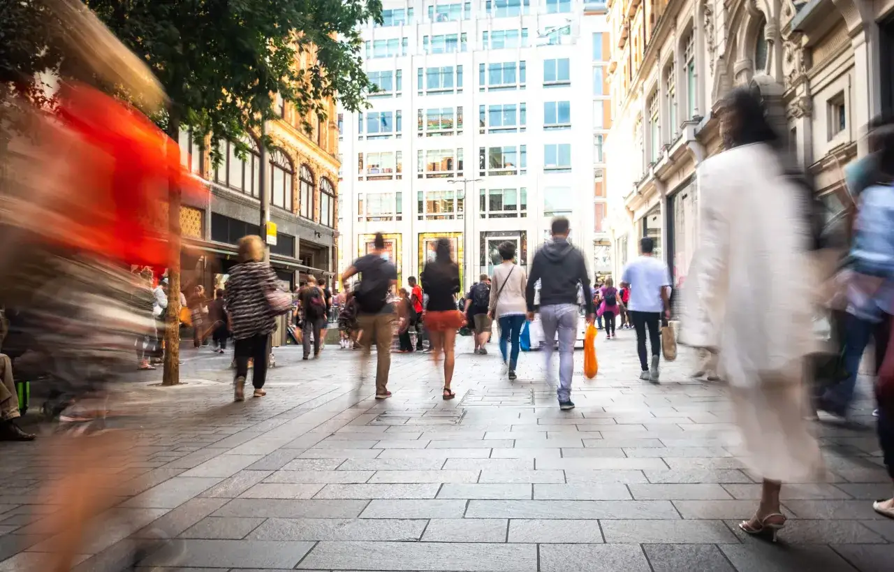 Dynamiczna fotografia uliczna uchwyciła ruch miejskiego tłumu. Ludzie spieszą się ulicą, tworząc rozmyte plamy kolor&oacute;w.